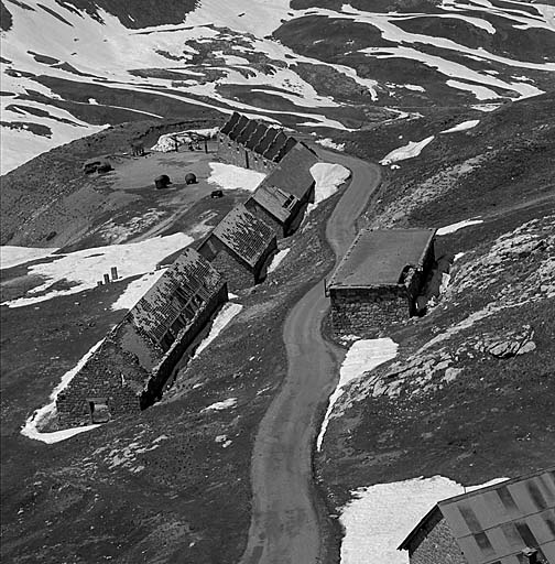 Partie basse du site vue du nord-est. Au premier plan, en bas, à droite, partie du bâtiment l. A droite de la route, bâtiment k. A gauche, de bas en haut, écuries i, j, g et h. Sur le terre-plein, cuirassements en dépôt.