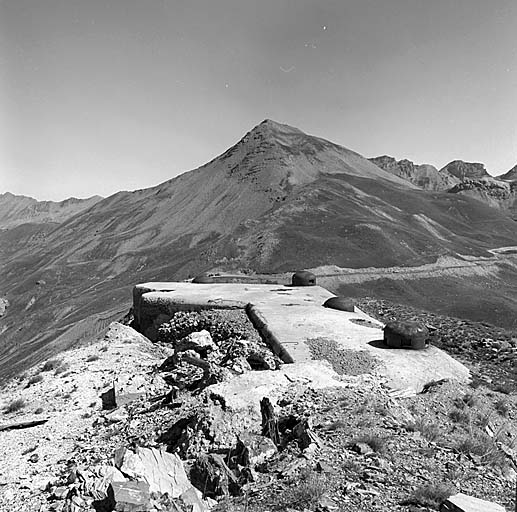 Bloc 2. Vue d'ensemble du dessus prise du sud-ouest. En premier plan, de gauche à droite : 1 : cloche JM battant le col. 2 : cloche GFM à 3 créneaux. 3 : cloche JM battant la Haute Tinée. 4 : cloche GFM de défense du dessus. Au second plan, à gauche, vallon des Granges Communes col et route D64 descendant vers les Fourches. Au fond, la cime de Voga.