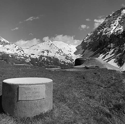 Dessus de l'ouvrage vus vers l'avant. Au premier plan, table d'orientation avec inscription commémorative. A droite, la cloche du bloc 4 vue de profil. Au fond, le col du Vallonet, à droite, les rochers de Saint-Ours.