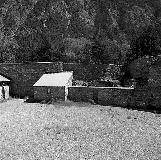 Vue arrière du saillant est prise de l'intérieur de l'ouvrage avec, de gauche à droite, l'extrémité du hangar a, le bâtiment d, et le mur d'isolement masquant le magasin à poudre e.