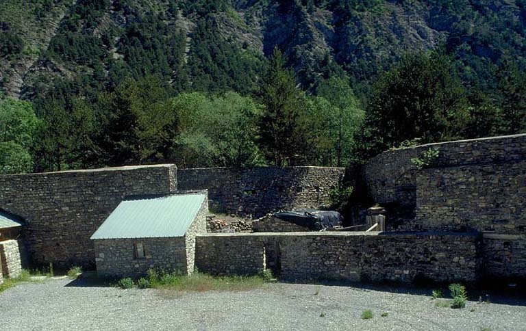 Vue arrière du saillant est prise de l'intérieur de l'ouvrage avec, de gauche à droite, l'extrémité du hangar a, le bâtiment d, et le mur d'isolement masquant le magasin à poudre e.