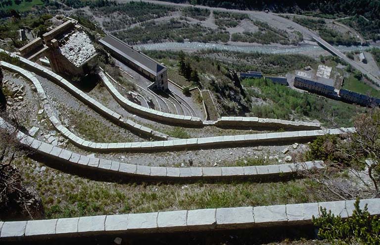 Fort supérieur. Vue plongeante des rampes descendant du fort moyen. A gauche la porte d'entrée arrière. Au centre et en contrebas, le bâtiment B (pavillon d'officiers). Au fond, la vallée de l'Ubaye et le pied des pentes de la Silve.