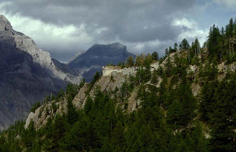 Vue d'ensemble de l'ouvrage prise de l'arrière, depuis la route d'accès. Au fond, à gauche, les rochers de Saint-Ours. Au centre, la Rocca Bianca.