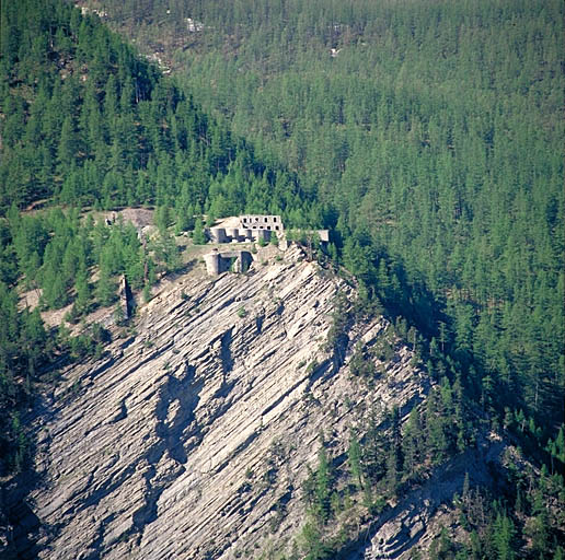 L'ouvrage (flanc gauche) vu depuis le haut de Saint-Ours, à 1600 m de l'autre côté de l'Ubayette. Au sommet de la falaise, le bloc 6. Derrière, le bloc 5 et le casernement de temps de paix. A gauche, le fossé vu en enfilade. A droite, le ravin de Siguret.