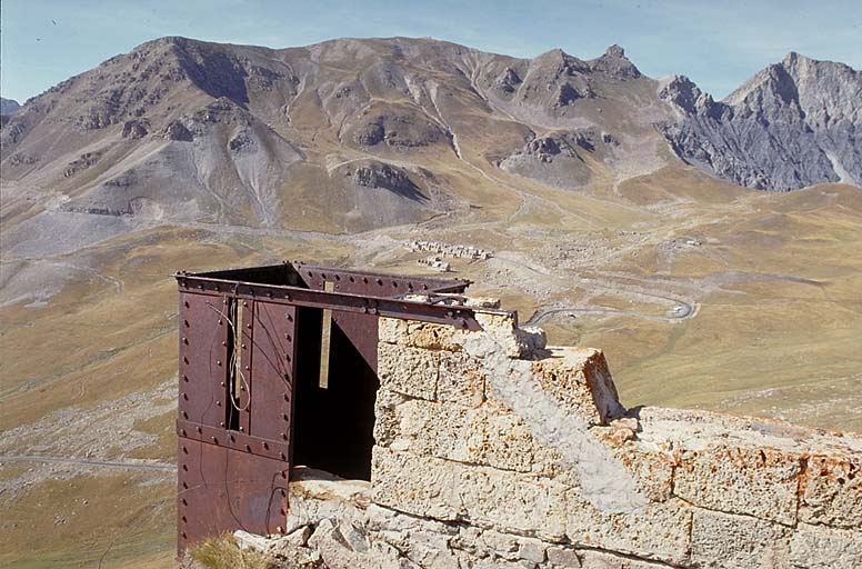 Blockhaus 3. Vue prise de la terrasse vers le nord-ouest. Au premier plan, l'échaugette d'angle et le parapet du pignon nord. A l'arrière plan, au centre, blockhaus de la Pelousette et à droite sommet du Bonnet Carré. Dans la cuvette, camp des Fourches et route de Nice.