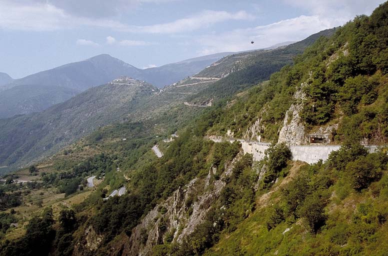 Vue de situation prise de la direction de la Bollène vers le sud-ouest. A droite, la D 2565 et la casemate active de l'ouvrage. A gauche, la vallée de Bramafam dominée, au centre, par l'ouvrage de Rimplas au sommet du piton de la Madeleine.