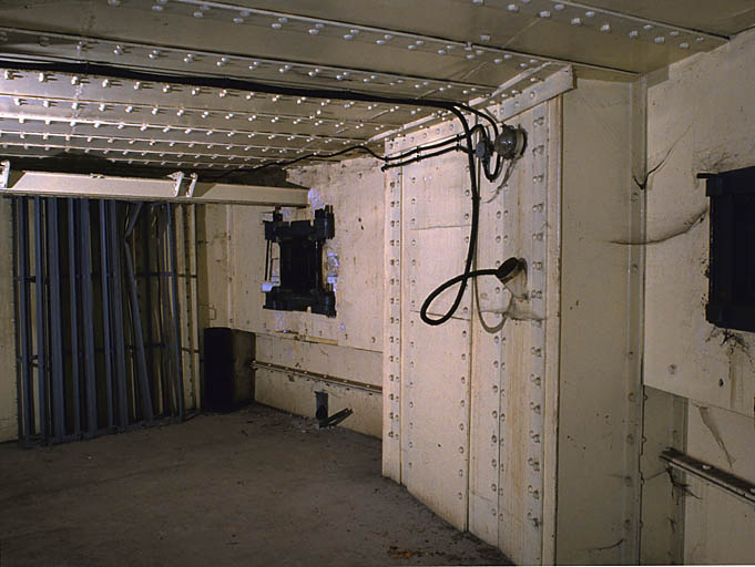 Casemate active (bloc 3). Vue intérieure. De gauche à droite : casiers à munitions. Bac de refroidissement des mitrailleuses. Créneau de gauche avec birail porteur du canon de 47 mm. Goulotte lance-grenades. Créneau de droite (JM).