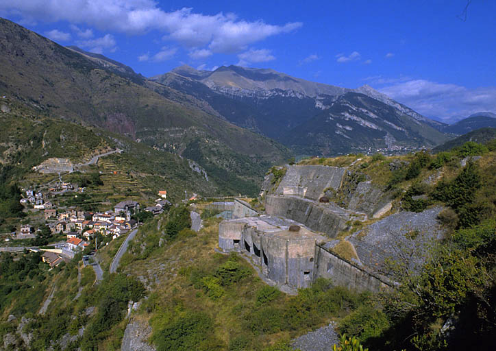 Versant nord-ouest vu du sud-ouest. Au premier plan, escarpement et bloc 4 (casemate "Tinée"). Plus loin, le village. Au fond, crête de l'ancienne frontière.