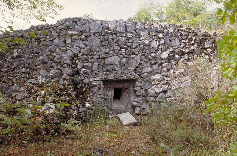 Casemate double de mitrailleuse. Créneau de gauche. Vue extérieure rapprochée. Remarquer le camouflage en pierres rapportées simulant un mur de pierres sèches. ; Ouvrage de Castes Ruines, casemate de mitrailleuse avec camouflage en pierres rapportées simulant un mur de pierres sèches.