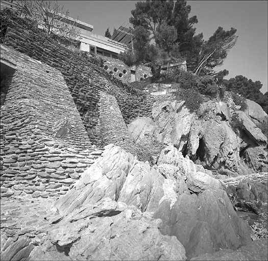 Vue d'ensemble du mur de soutènement du jardin avec la façade sud à l'arrière plan, depuis le bord de mer.