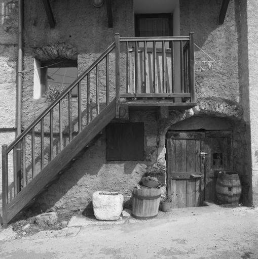 Village. Parcelle 263, façade sud. Sous le balcon pierre à huile ou à fromages datée de 1885, benne à vendange et tonneaux.