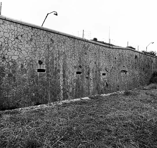 Front sud-est. Vue extérieure prise de la contrescarpe. Dans l'escarpe, soupiraux du bâtiment m et, à l'extrême droite, créneau de pied.