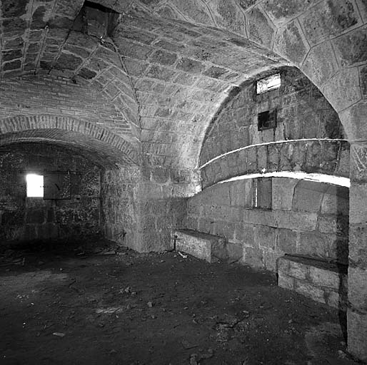 Aile gauche du bâtiment a. Premier sous-sol, local 7 (chambre de tir triple). Vue intérieure. A gauche, embrasure battant la pente en contrebas de la route. A droite, embrasure tirant sur le col d'Eze et créneau de pied. A la clef : cheminée de ventilation.