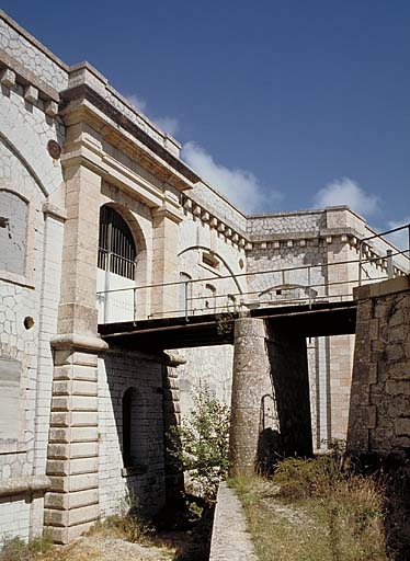 Aspremont, fort du Mont Chauve. ; Front de gorge. Partie centrale du bâtiment a vue de la branche gauche du fossé. Au centre, l'entrée du fort et le pont d'accès. Sous l'entrée, la poterne donnant dans le fossé.