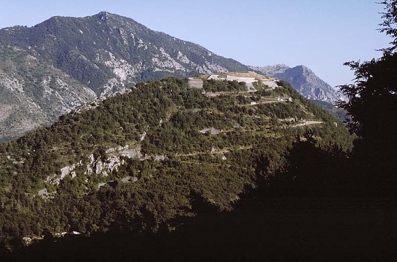 Vue lointaine du fort et de la route d'accès prise de la D 2204, en descendant du col de Braus, au nord-ouest. Derrière, ensemble Plan Germain-Mont Razet.