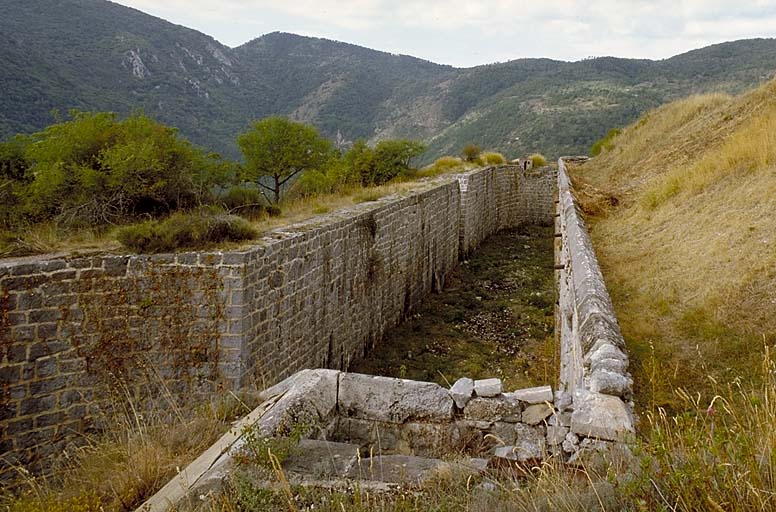 Front sud. Vue du fossé prise d'enfilade du haut de la caponnière sud. A gauche, dans la contrescarpe, en fond de fossé, entrée du colombarium et, à côté, échancrure de contrescarpe. Au fond, abri et guérite observatoire du saillant sud-ouest.