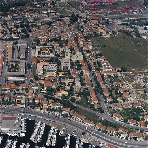 Partie orientale. Vue aérienne du secteur situé entre l'allée Sacoman et le boulevard Fenouil, prise du sud en direction du nord : au premier plan le port et la voie littorale, au lointain le quartier de la gare et les voies ferrées. Au centre les ensembles d'immeubles résidentiels construits après 1960 sur des terrains longtemps gelés par des tuileries et des exploitations agricoles.