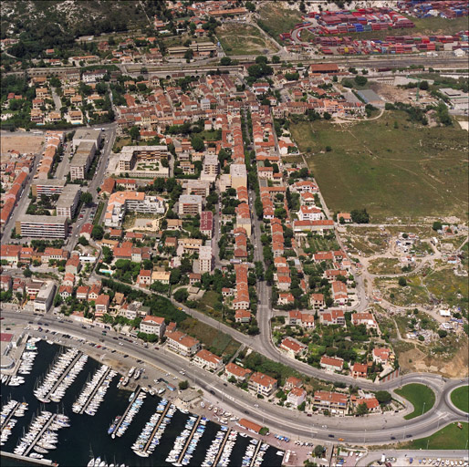 Vue aérienne du boulevard Fenouil prise du sud en direction du nord. Au premier plan le port, le chemin du Littoral (RN 568b) et le secteur de la Reconstruction, à l'arrière-plan le quartier de la gare.