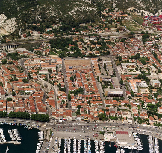 Vue aérienne de situation prise du sud en direction du nord. Au premier plan le port et la section du chemin du Littoral dite Plage de l'Estaque (RN 568b), à l'arrière-plan le piémont de la colline et la voie ferrée. Le lotissement est délimité à gauche par le tracé en S du boulevard Roger-Chieusse qui sépare également les quartiers de l'église et de la Fontaine-des-Tuiles. A droite, le long de la rue Emile-Rouvière qui limite le lotissement vers l'est, les ensembles d'immeubles construits dans les années 1970 occupent l'emplacement d'anciennes tuileries.