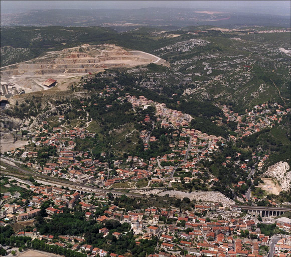 Vue aérienne des collines au-dessus des voies ferrées, prise du sud en direction du nord : carrière de la cimenterie Lafarge à gauche au lointain, Piches et la Falaise au centre, le vallon du Marinier dans le lointain à droite.