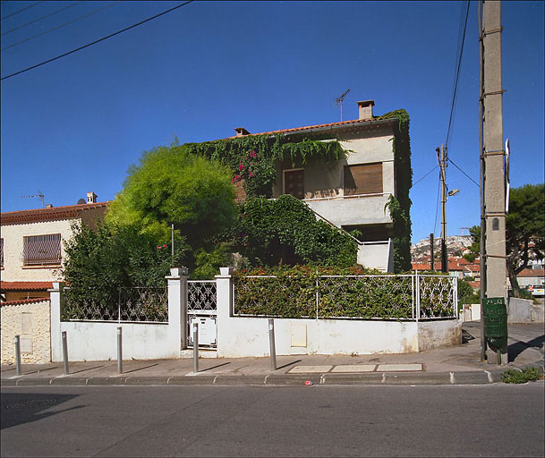 Vue générale de la façade ouest prise du boulevard Albin-Bandini, clôture et jardin au premier plan.