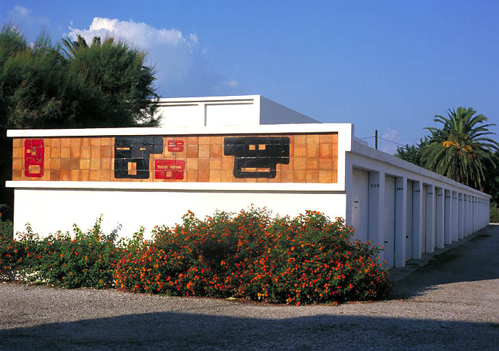 Garages situés à l'entrée de la résidence. Façade sud-ouest : décor de céramique.