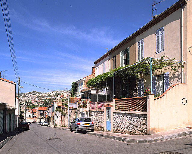 Vue en perspective de la partie haute de l'îlot, depuis l'angle de la rue Emile-Rouvière, en direction du boulevard Roger-Chieusse. Maisons en retrait avec remises en soubassement et terrasses. A l'arrière-plan, les collines des Riaux.