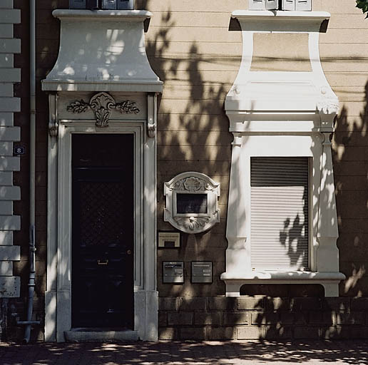Vue partielle de la façade ouest montrant le bossage en soubassement, les agrafes au-dessus des baies, l'encadrement de la plaque de bronze.