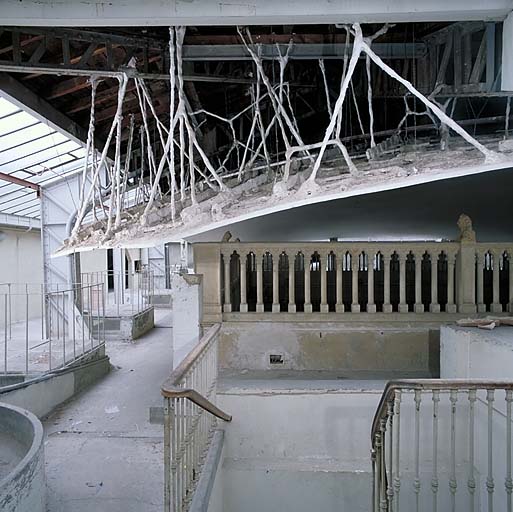 Vue intérieure: la fausse coupole en plâtre du patio suspendue à la charpente métallique par des filins, vue de profil.