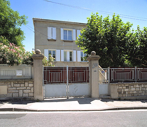 Vue prise depuis la rue du mur-bahut de clôture, des portail et de la façade de la maison.