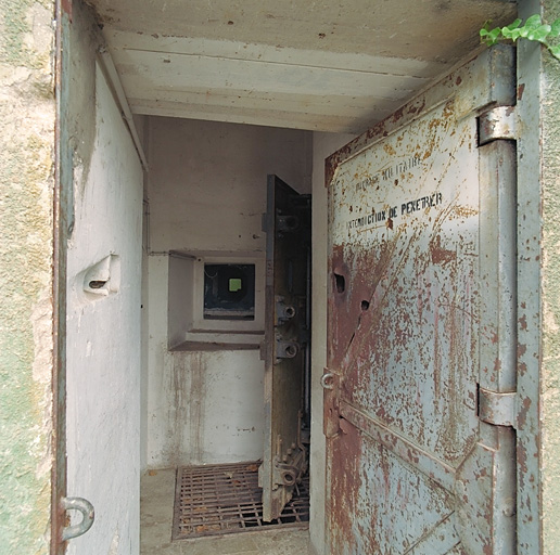 Façade du bloc d'entrée 1, détail de la porte des hommes ouverte, couloir en chicane flanqué d'un créneau.