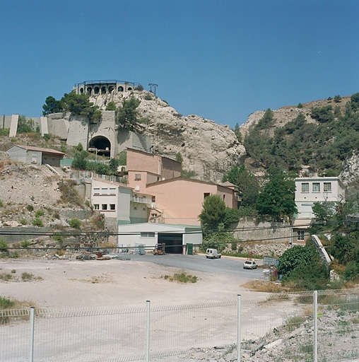 Chemin de la Nerthe, Vallon des Riaux. Au premier plan, emplacement de l'usine démolie, à l'arrière logements liés à la cimenterie, à gauche rotonde trémie support de tapis roulant.