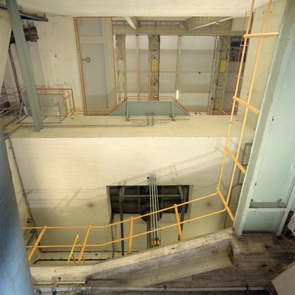 Vue en contre-plongée du hall des machines depuis le niveau des conduites forcées. Vue de l'arbre sous l'alternateur du groupe 1. En partie haute, les deux ponts-roulants de 35 tonnes.