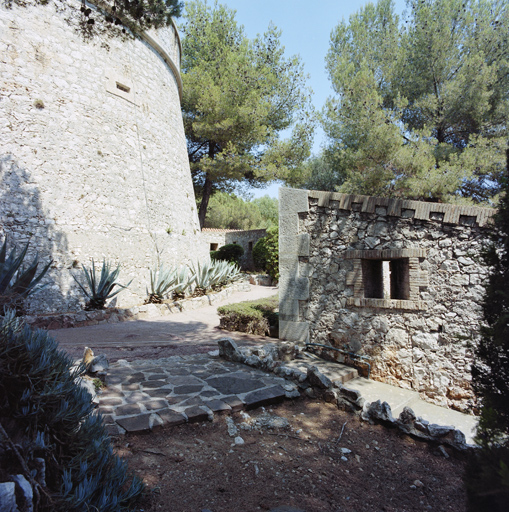 Mur de clôture crénelé de l'enceinte chemisant le pied de la tour.
