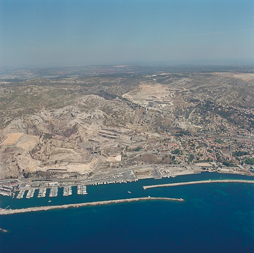 Vue aérienne prise du sud du massif de la Nerthe avec les zones de carrières et les emplacements d'anciennes industries. Au premier plan, la route du littoral et les aménagements littoraux.