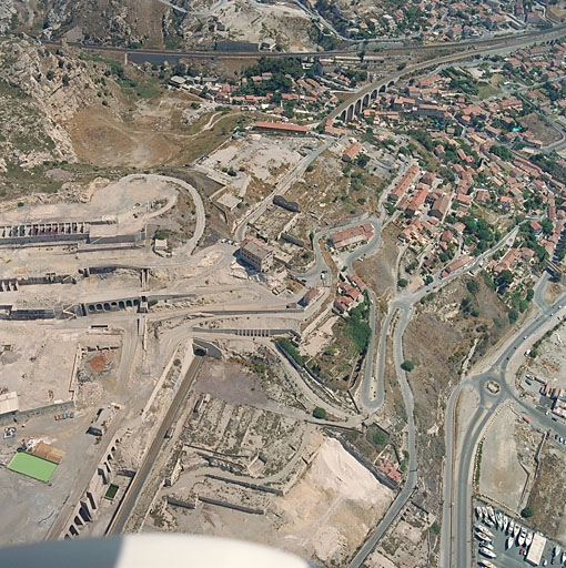 Vue aérienne d'ensemble du quartier prise de l'est. Au premier plan, le site de Rio Tinto, au second plan, s'étageant sur le versant de la colline, l'agglomération des Riaux, au 3e plan, les voies ferrées et le secteur du Vallon des Riaux.