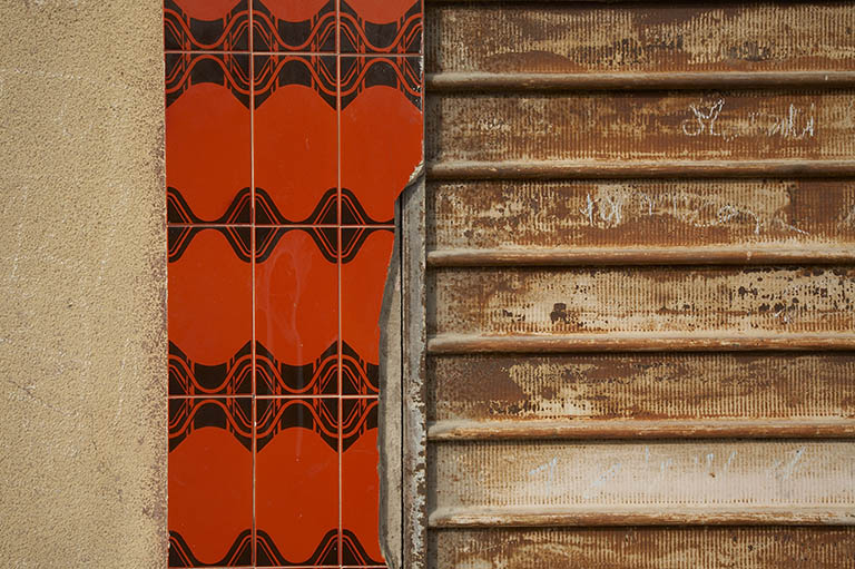 Détail de la devanture de magasin : placage de céramique rouge, rideau métallique.