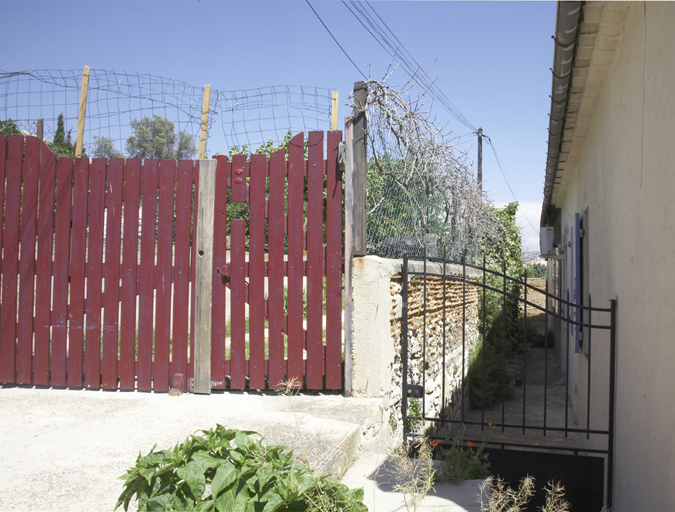 Passage à l'arrière des immeubles à logements avec grille sur l'allée d'accès à la campagne.