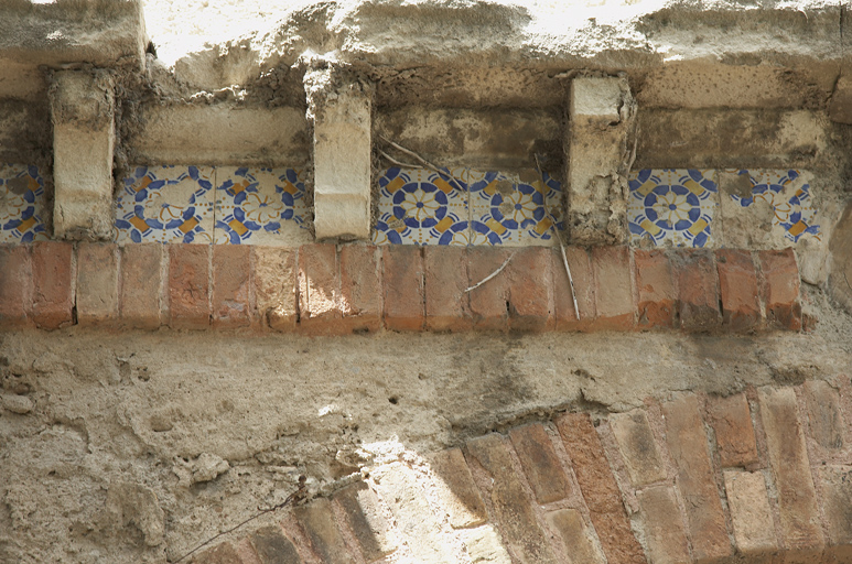Balustrade de la terrasse : détail. Carreaux en céramique entre corbeaux en pierre, au dessus d'un lit de briques pleines.