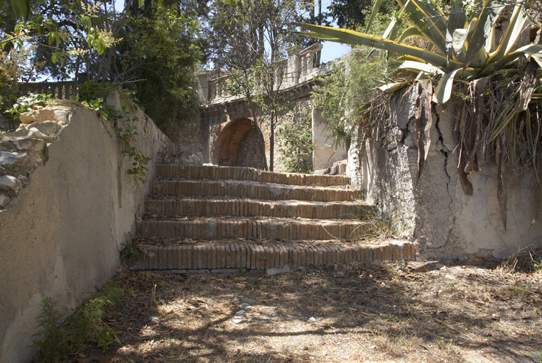 Escalier de jardin allant à la terrasse devant le mur de soutènement à arcatures aveugles.
