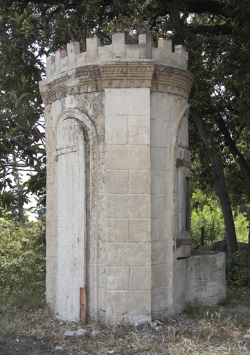 Puits couvert à décor en rocaille en forme de tour crénelée : porte entrebaillée en trompe l'oeil.