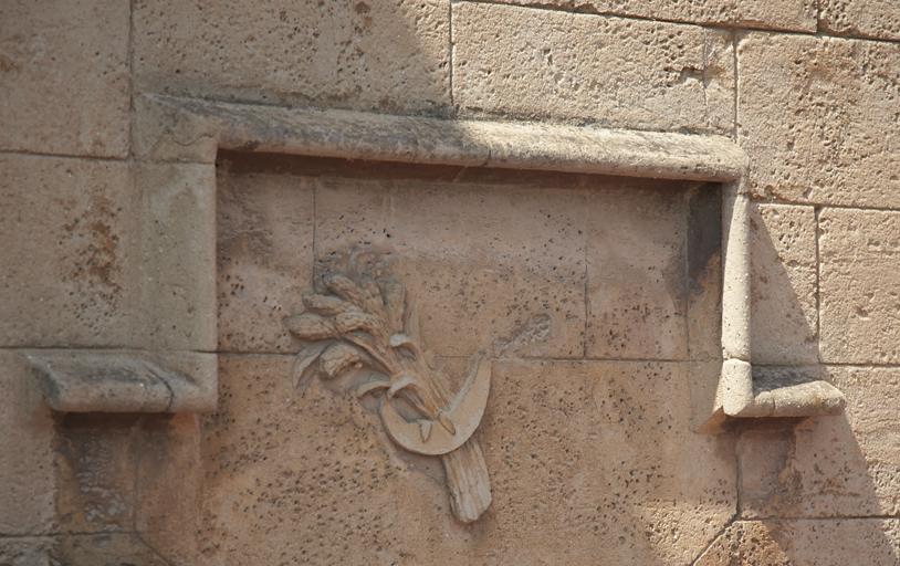 Epis de blé et serpe en rocaille sur la façade des communs.