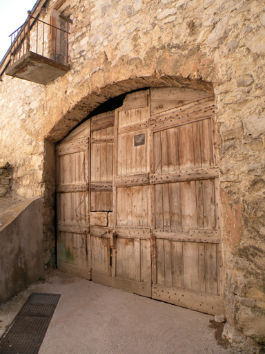 Bâtiment 2. Elévation ouest, premier niveau. Porte de l'écurie-remise. ; Porte de remise : encadrement en arc segmentaire en pierre de taille de tuf ; meuniserie à vantaux articulés (Vergons).