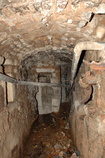 Vue prise du sud sur le canal de fuite de la roue à eau, débouchant à droite, en haut de la chambre hydraulique du moulin inférieur (baie bouchée) et à gauche sur la citerne en pierre de taille.