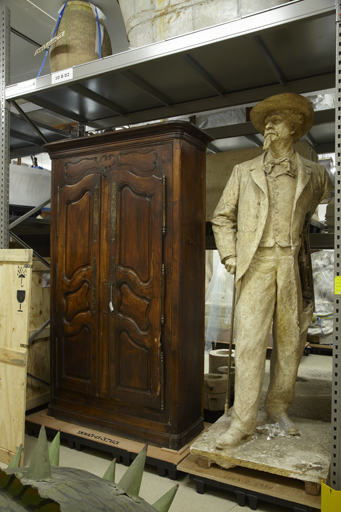 Vue de la réserve consacrée aux objets encombrants et sculptures, vue rapprochée sur une sculpture représentant Frédéric Mistral et une armoire provençale.