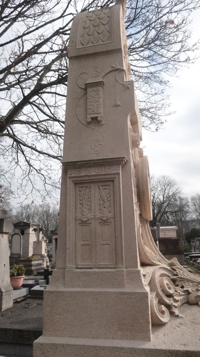 détail de la face latérale gauche : reliefs représentant la petite porte du Panthéon avec le monogramme S.G. (Sainte-Geneviève), et le Gril de saint Laurent avec le monogramme S.L. en référence à la restauration du portail de l’église Saint-Laurent à Paris menée par Constant-Dufeux