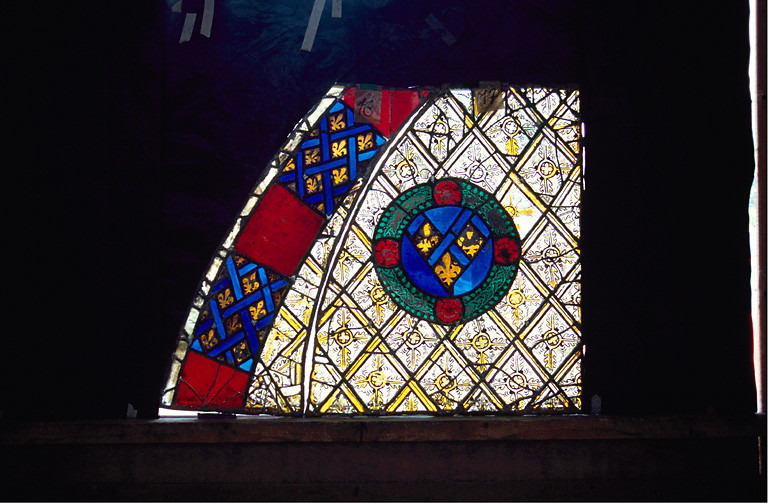 verrière : Panneaux 16, 17 (Ap. R.) bordure entourée d'un filet blanc, alternance de motifs rouges et bleus ; quadrillage tracé au jaune d'argent sur ce fond se détache des couronnes de feuilles vertes agrémentées de quatre roses rouges.