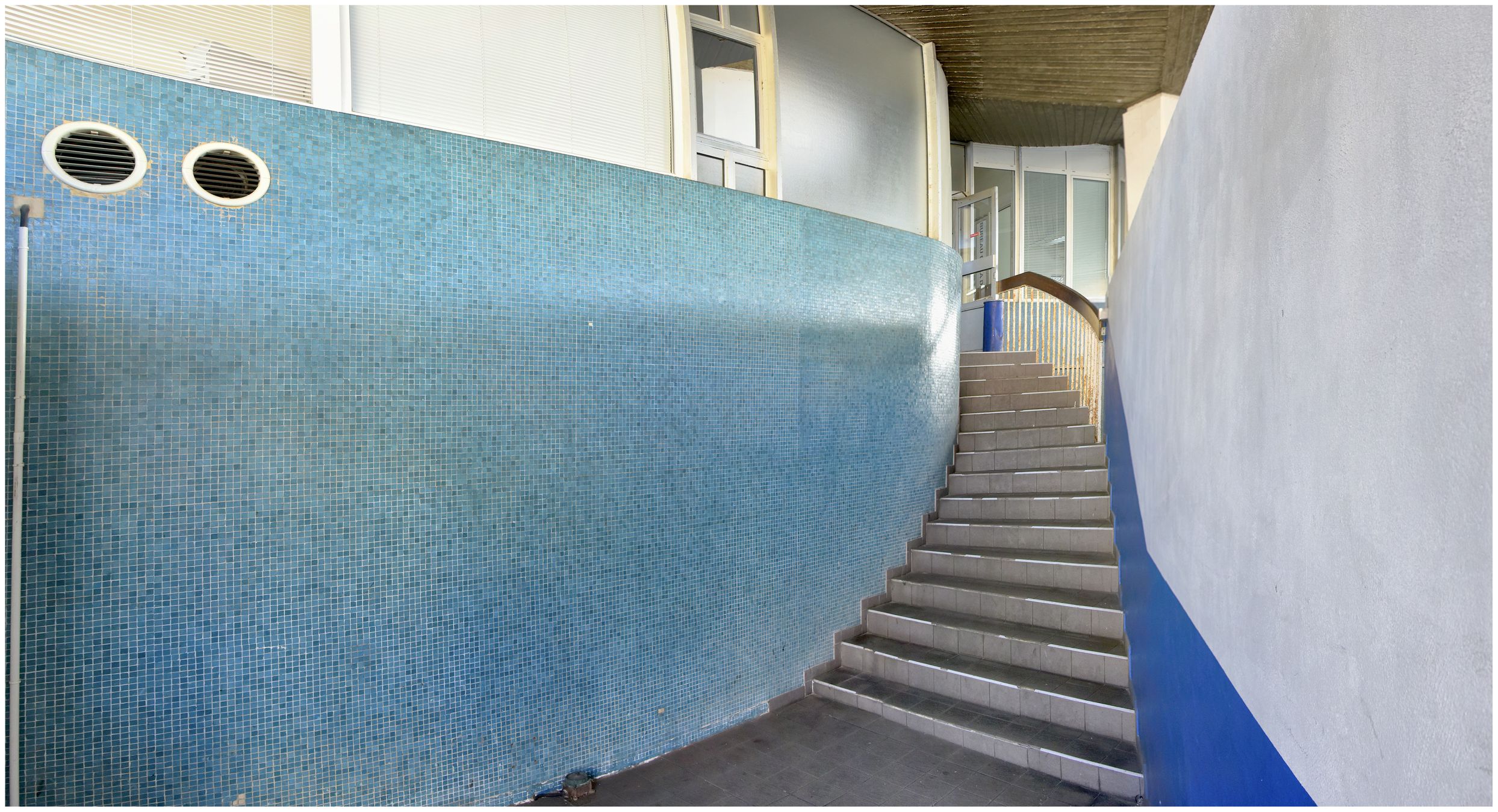 Escalier d’accès à la salle de la criée. Mur arrondi revêtu de petits carreaux de céramaque bleus.