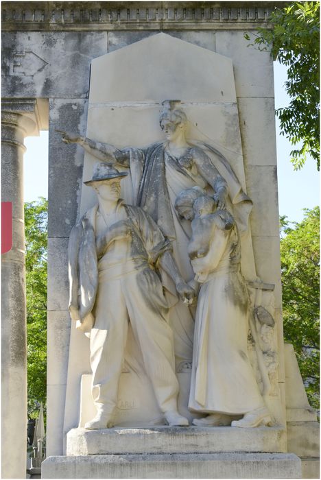 Groupe sculpté de gauche. Le départ : un homme en civil quitte une femme avec enfant, ils sont surmontés par une figure coiffée de la Maison Carrée représentant la ville de Nîmes, qui transmet l’appel de la patrie d’un geste impérieux pour l’homme et protecteur pour la femme.