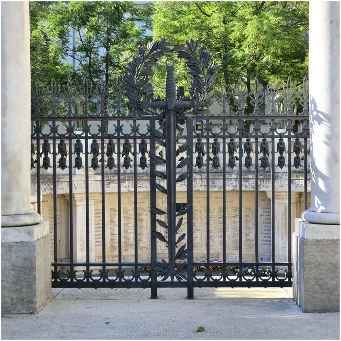 Accès à la crypte, fermé par une porte en fer forgée à deux battants décorée en son centre d'une épée surmontée d'une couronne de lauriers, œuvre de Tréchard.